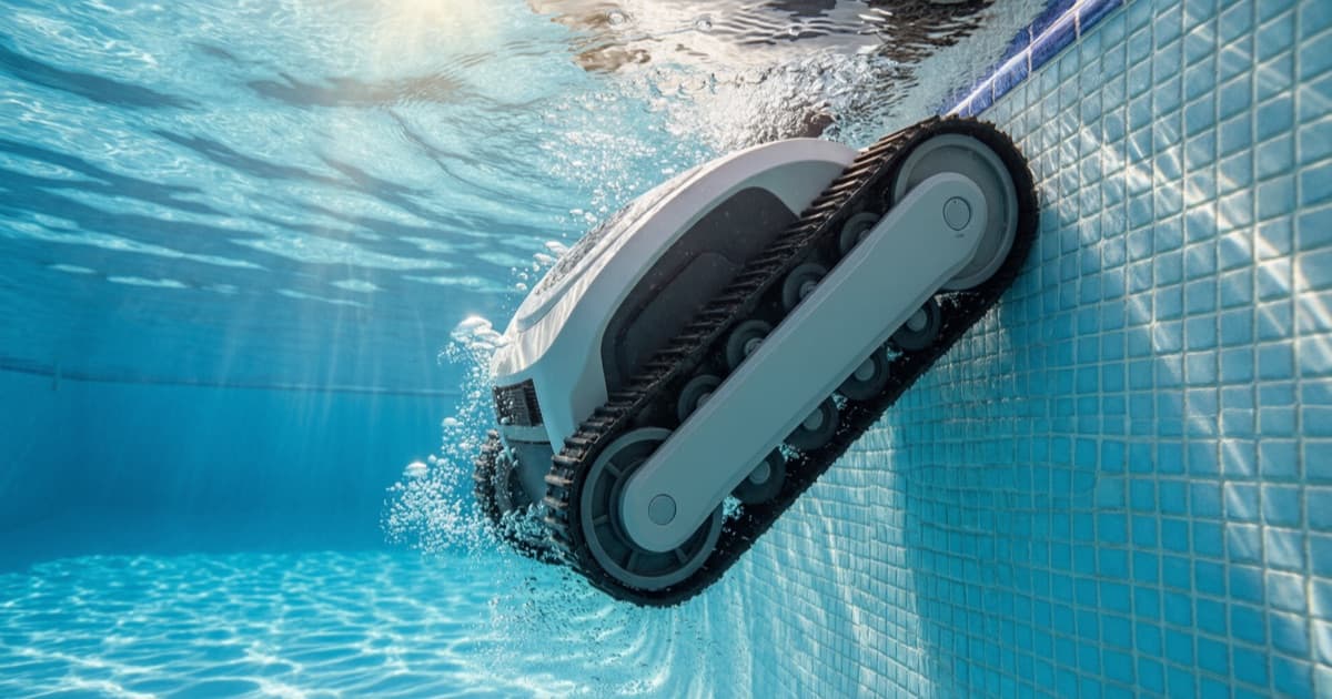 A tracked robotic pool cleaner climbing the tiled wall of a clear blue pool